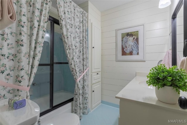 bathroom with combined bath / shower with glass door, vanity, toilet, and wooden walls