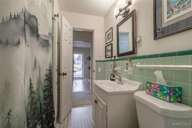 full bathroom with tile walls, a shower with shower curtain, toilet, wainscoting, and vanity