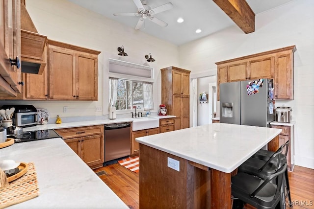 kitchen with light wood-style flooring, beam ceiling, stainless steel appliances, and a sink