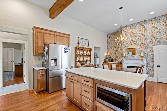 kitchen with light wood finished floors, beamed ceiling, decorative light fixtures, stainless steel appliances, and a fireplace