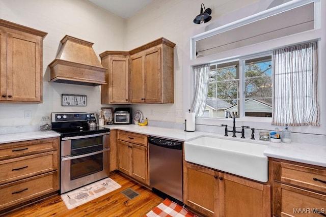 kitchen featuring brown cabinets, custom exhaust hood, stainless steel appliances, dark wood-type flooring, and a sink