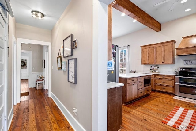 kitchen with stainless steel appliances, wood-type flooring, light countertops, and custom range hood