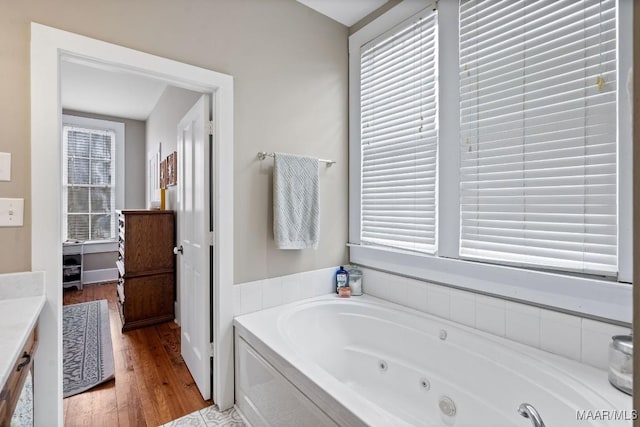 full bath featuring a jetted tub, vanity, and wood finished floors