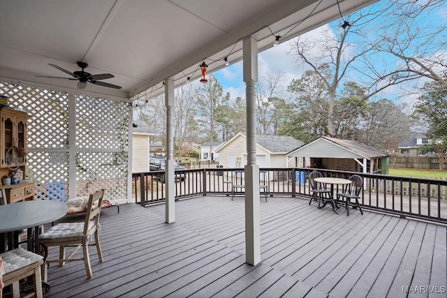 wooden terrace with outdoor dining area, ceiling fan, and an outdoor structure