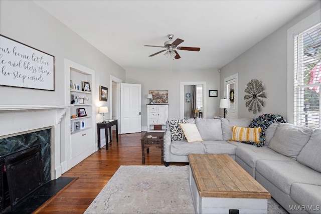 living room featuring built in features, dark wood-style flooring, a fireplace, and a ceiling fan