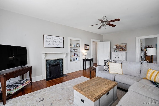 living room featuring built in shelves, a premium fireplace, ceiling fan, wood finished floors, and baseboards