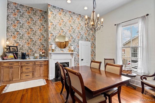 dining area with a fireplace with flush hearth, hardwood / wood-style flooring, and a notable chandelier