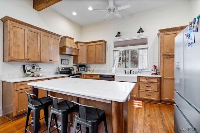 kitchen with wood-type flooring, custom range hood, brown cabinets, stainless steel appliances, and a sink