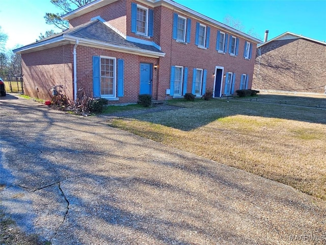 view of front of home featuring a shingled roof, a front yard, and brick siding