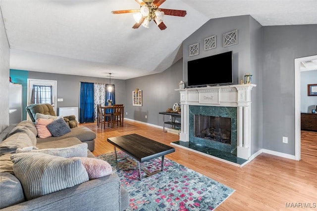 living area with a high end fireplace, vaulted ceiling, baseboards, and wood finished floors