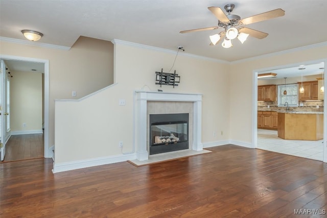 unfurnished living room featuring a sink, baseboards, ornamental molding, light wood finished floors, and a tiled fireplace