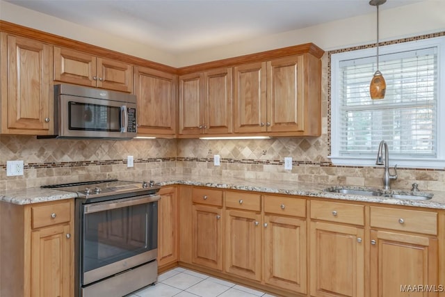 kitchen with tasteful backsplash, appliances with stainless steel finishes, a sink, and light stone countertops