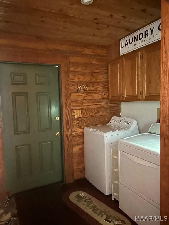 washroom featuring cabinet space, wood ceiling, wood walls, and washing machine and clothes dryer