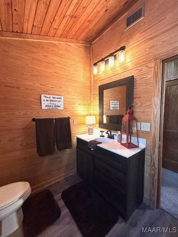 bathroom featuring visible vents, toilet, wooden ceiling, vanity, and wood walls