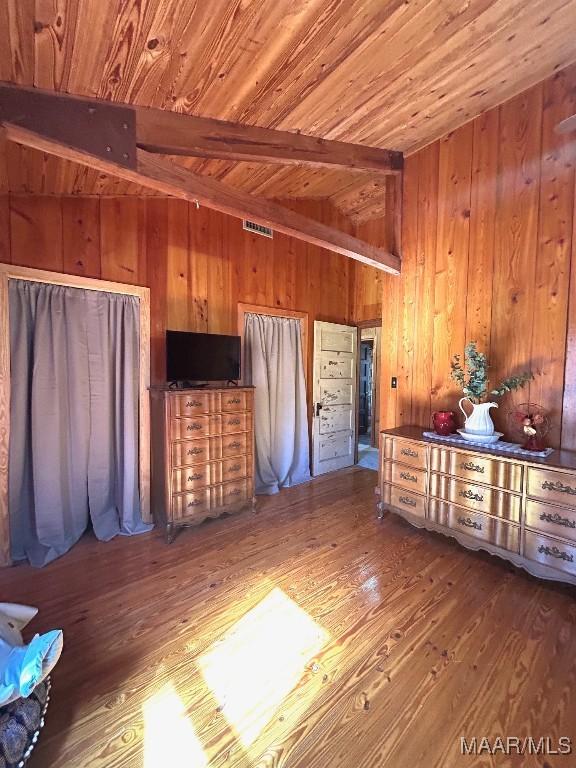 unfurnished bedroom featuring lofted ceiling with beams, wood finished floors, wood ceiling, and wooden walls