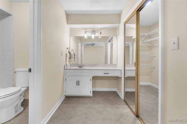 full bathroom featuring a walk in closet, toilet, vanity, tile patterned flooring, and baseboards