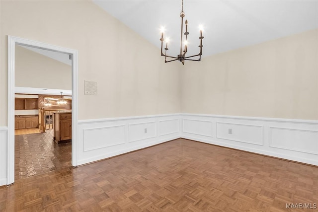 unfurnished room featuring wainscoting, vaulted ceiling, and an inviting chandelier