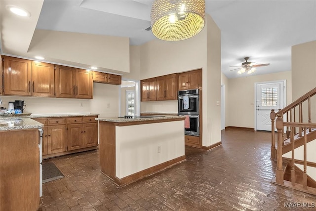 kitchen with baseboards, brown cabinetry, ceiling fan, brick floor, and stainless steel double oven