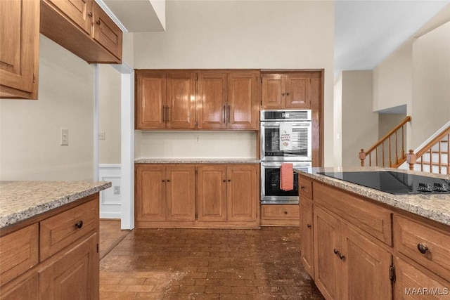 kitchen featuring brown cabinetry, light stone counters, brick floor, black electric cooktop, and stainless steel double oven