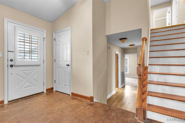 entryway featuring brick floor, plenty of natural light, baseboards, and stairs