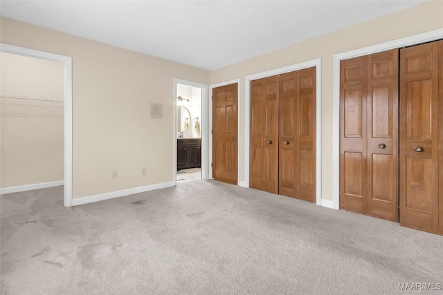 unfurnished bedroom with carpet floors, ensuite bathroom, baseboards, and two closets