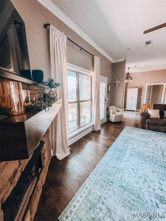 living area featuring a notable chandelier, wood finished floors, visible vents, and crown molding