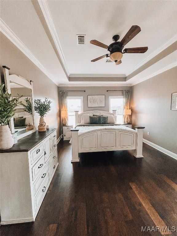 unfurnished bedroom with baseboards, visible vents, dark wood-type flooring, a tray ceiling, and crown molding