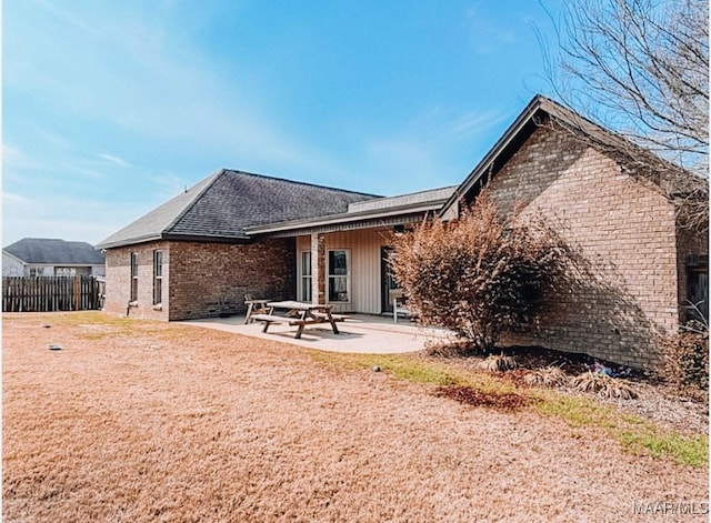 rear view of property with brick siding, a patio area, fence, and a shingled roof