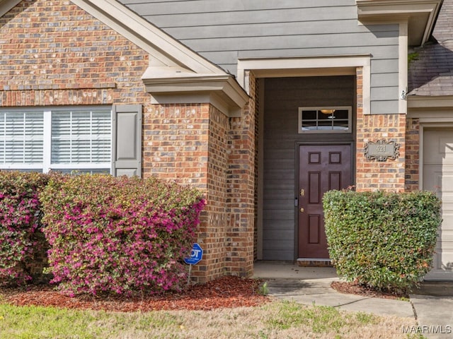 view of exterior entry featuring a garage and brick siding