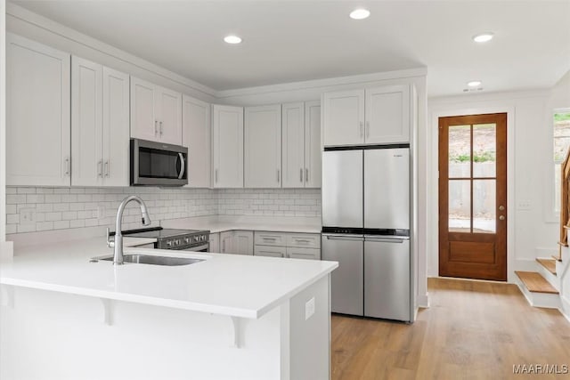 kitchen with light wood finished floors, a peninsula, stainless steel appliances, light countertops, and a sink