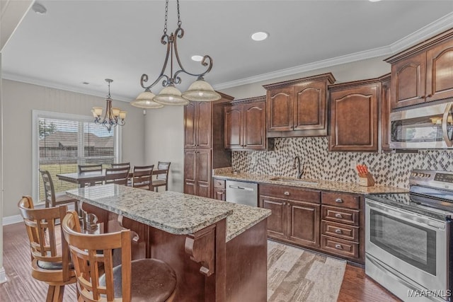 kitchen featuring stainless steel appliances, wood finished floors, a kitchen island, a sink, and crown molding