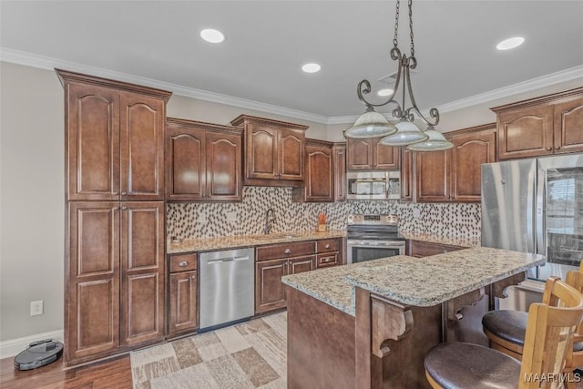 kitchen featuring light stone counters, a breakfast bar area, a sink, ornamental molding, and appliances with stainless steel finishes