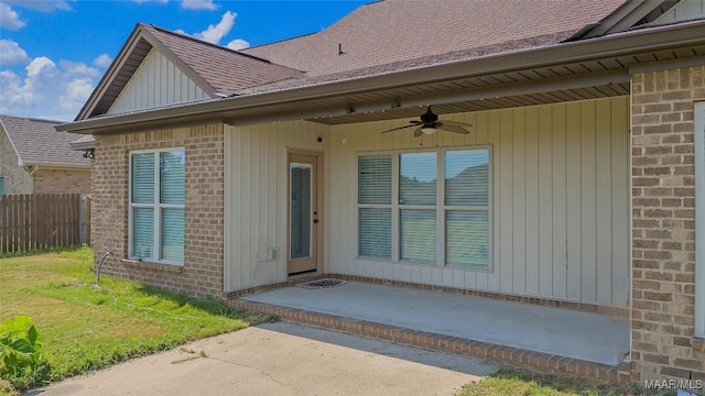 entrance to property with ceiling fan, brick siding, fence, roof with shingles, and board and batten siding