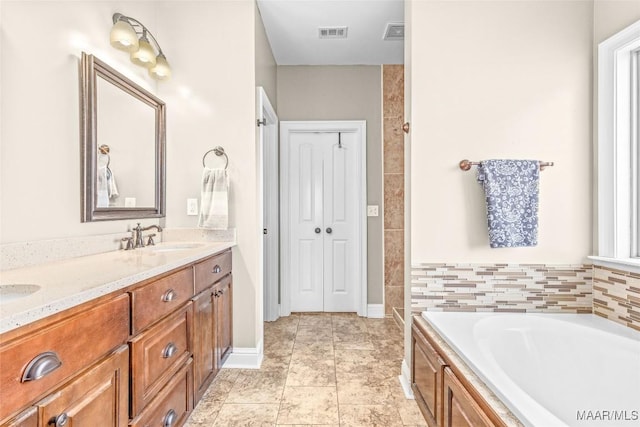 bathroom featuring a bath, double vanity, a sink, and visible vents