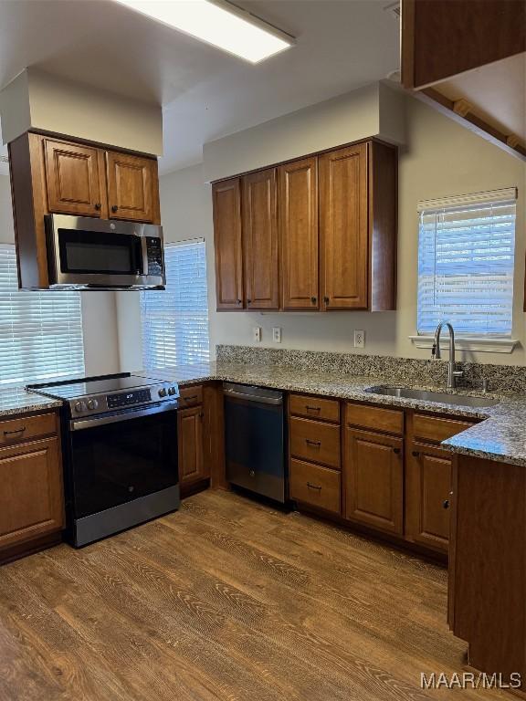 kitchen featuring dark wood-style flooring, a sink, appliances with stainless steel finishes, brown cabinetry, and dark stone countertops