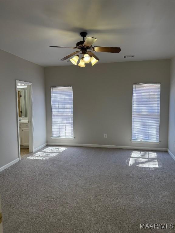 carpeted spare room featuring ceiling fan, visible vents, and baseboards