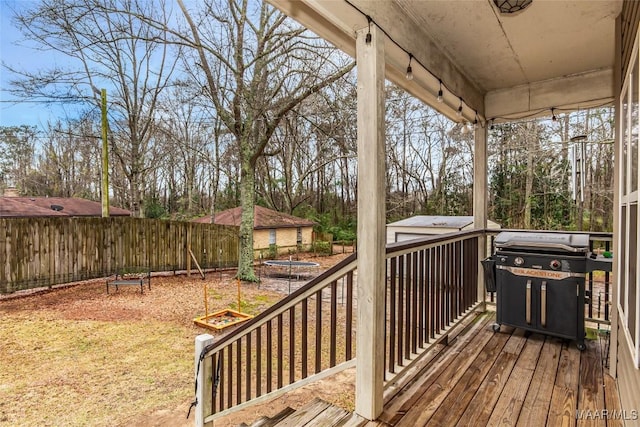 wooden terrace featuring a fire pit, area for grilling, a fenced backyard, an outbuilding, and a trampoline