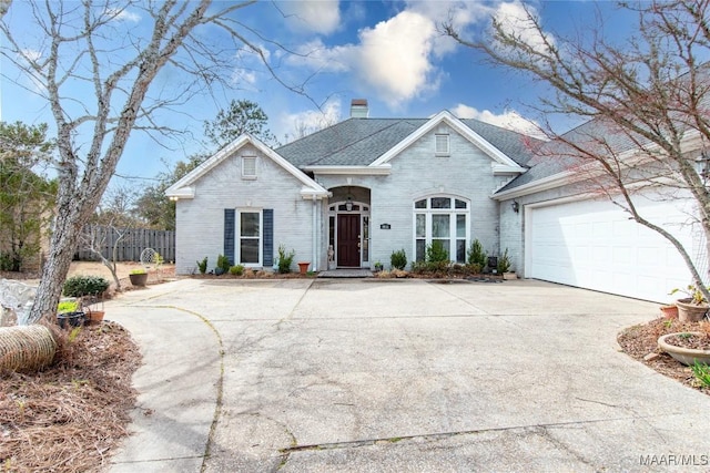 view of front of property featuring concrete driveway, brick siding, fence, and a chimney