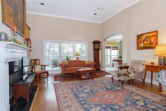 living area featuring arched walkways, a glass covered fireplace, a towering ceiling, ornamental molding, and hardwood / wood-style floors