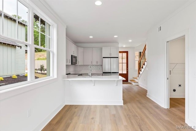 kitchen featuring a wealth of natural light, a sink, black microwave, stainless steel fridge, and a peninsula