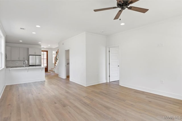 unfurnished living room featuring crown molding, stairway, light wood-style flooring, and baseboards