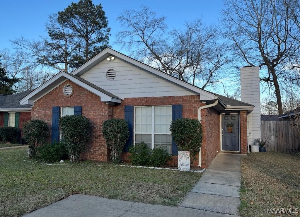 view of front of house featuring a front yard, a chimney, fence, and brick siding