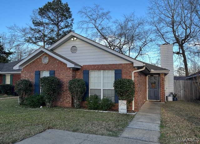 view of front of house featuring a front yard, a chimney, fence, and brick siding