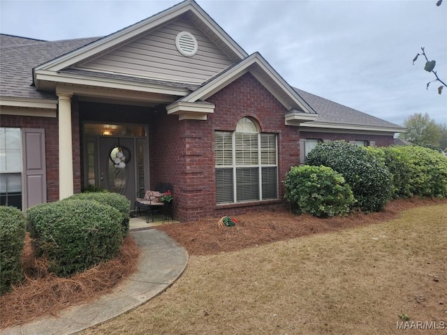 view of front of house with a shingled roof, a front yard, and brick siding