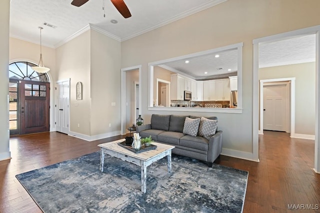 living room with dark wood-style flooring, visible vents, crown molding, and baseboards