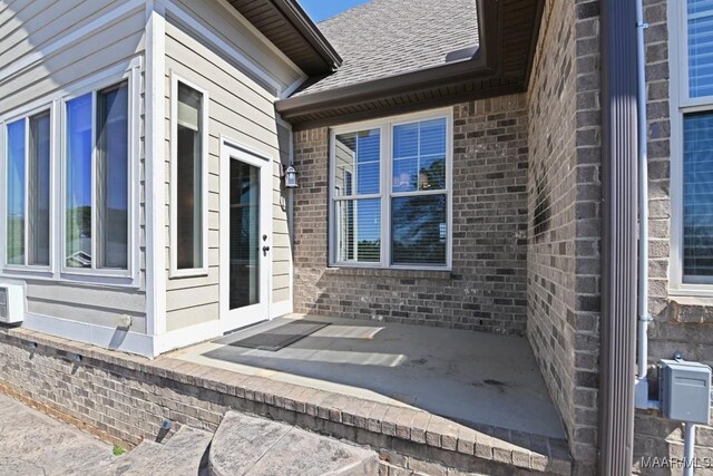 view of side of home with a shingled roof, brick siding, and a patio