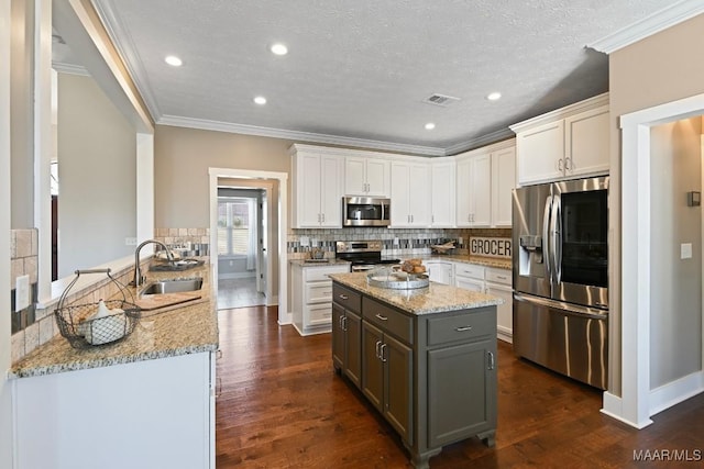 kitchen with crown molding, stainless steel appliances, tasteful backsplash, a sink, and light stone countertops