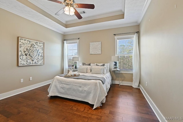 bedroom with multiple windows, a tray ceiling, hardwood / wood-style floors, and ornamental molding