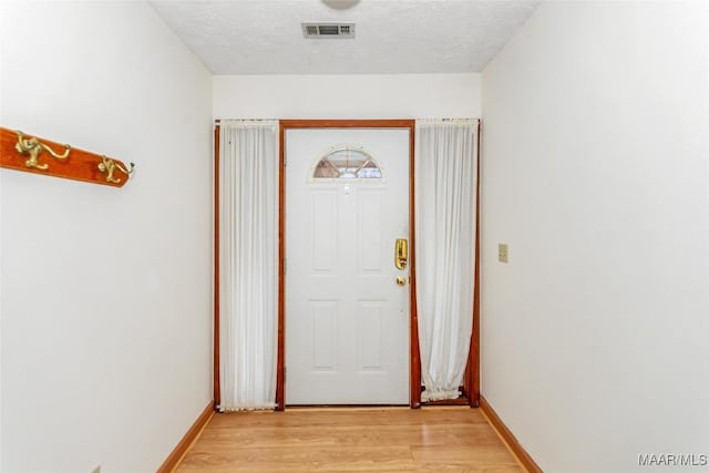 doorway to outside featuring light wood-style floors, baseboards, visible vents, and a textured ceiling