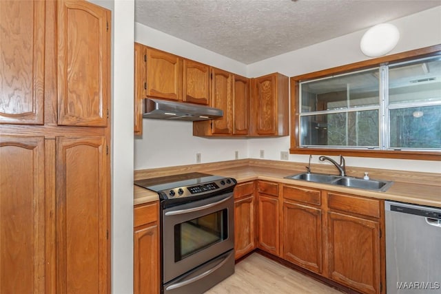 kitchen featuring appliances with stainless steel finishes, light countertops, a textured ceiling, under cabinet range hood, and a sink